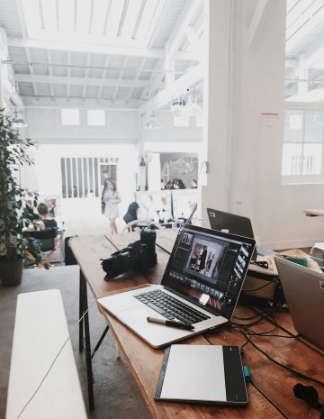 A bright, modern workspace featuring laptops, a camera, and a drawing tablet in an indoor office.